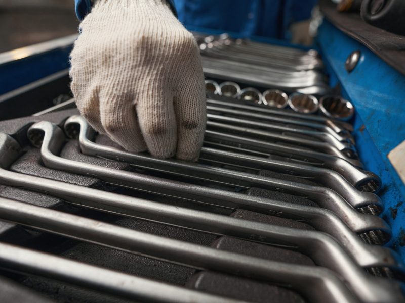 Close-up photo of male at service station Mechanic in protective gloves standing near the rack with tool and picking up keys for repairs